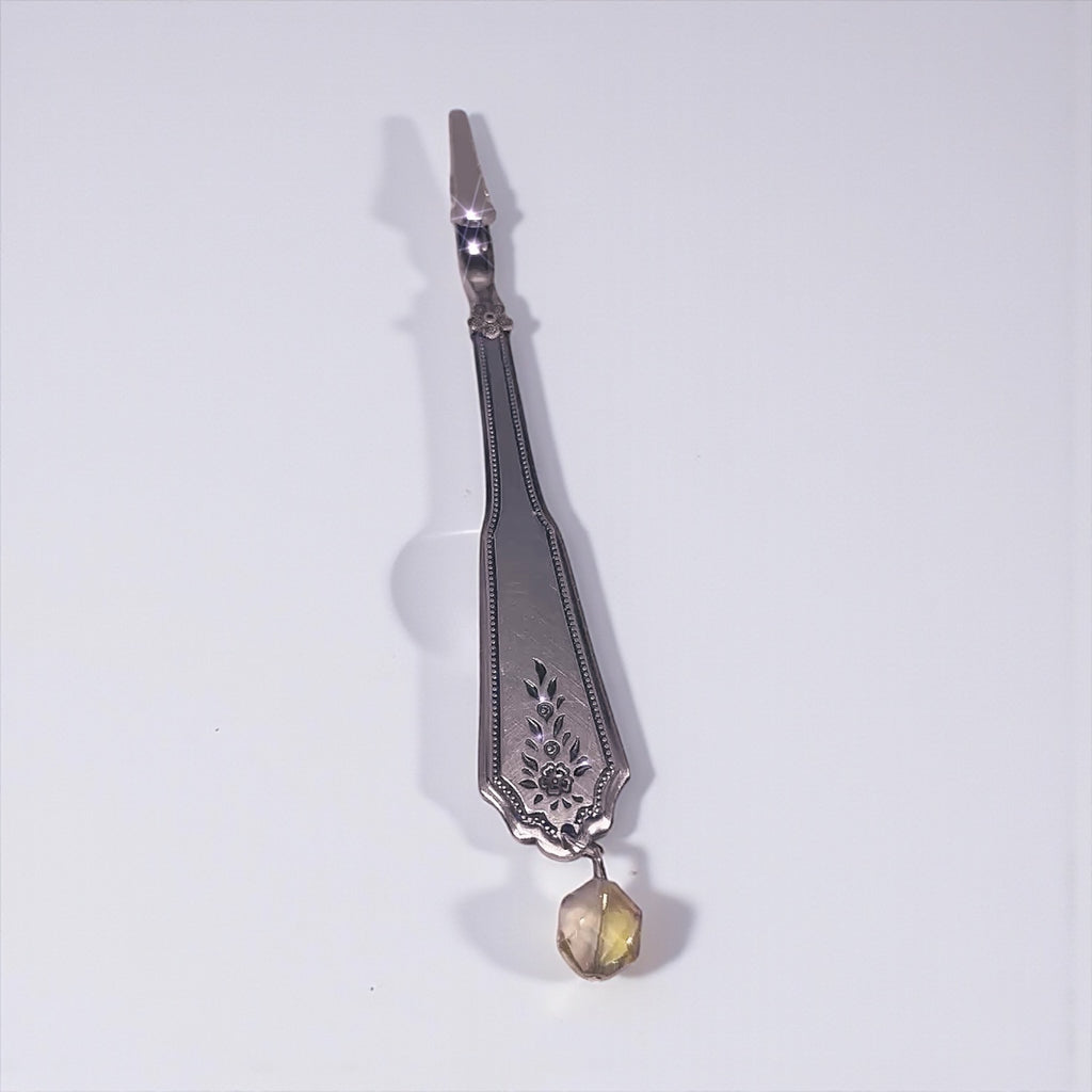 Decorative silver atm tool with a yellow gemstone on a white background