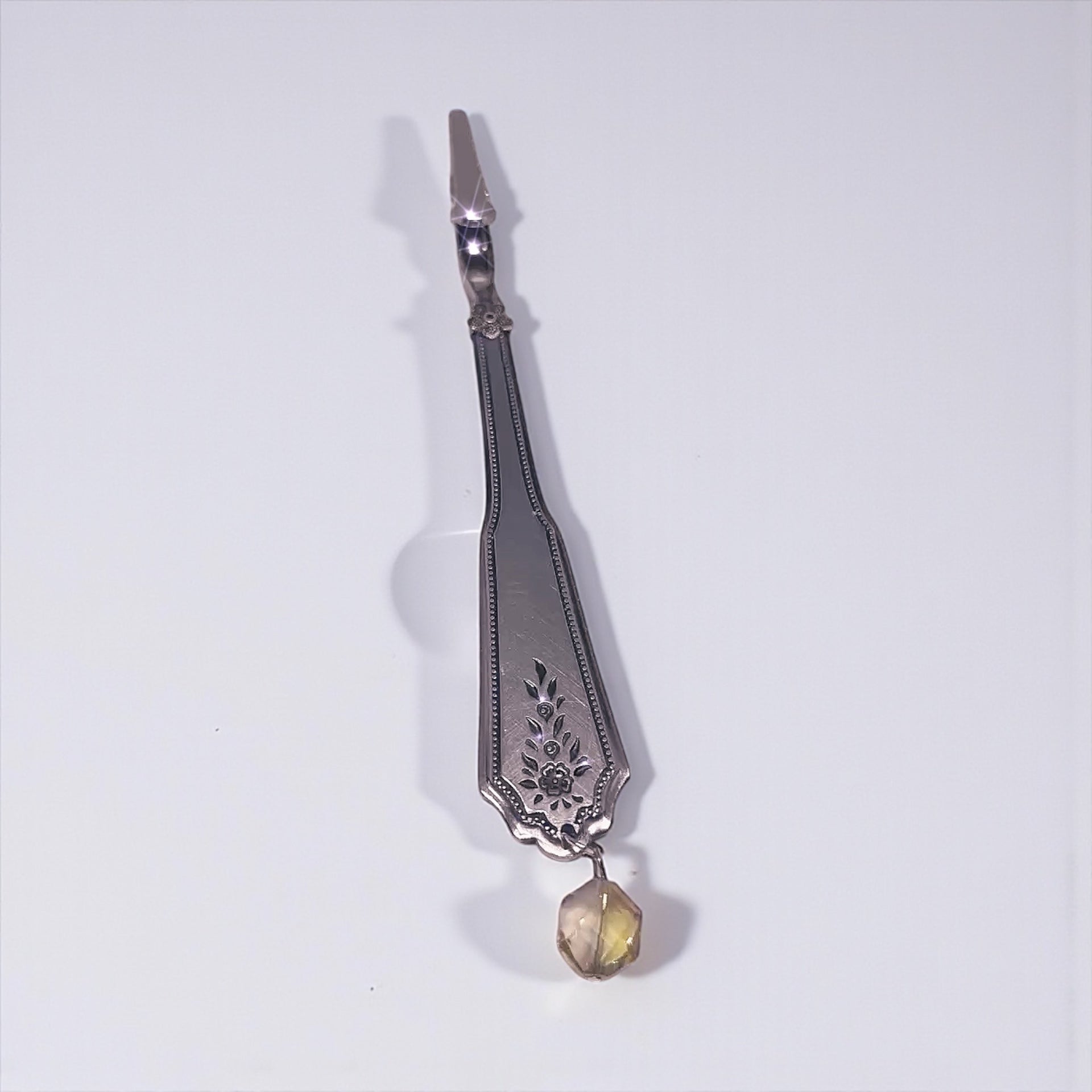 Decorative silver atm tool with a yellow gemstone on a white background