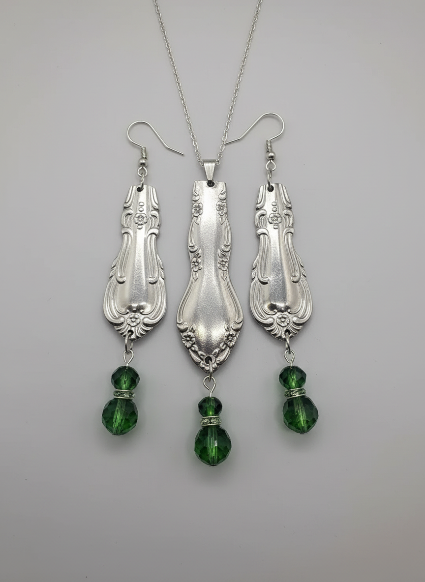 Silver spoon earrings with green gemstones on a black card.
