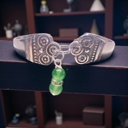 Silver bracelet with green beads on a dark surface