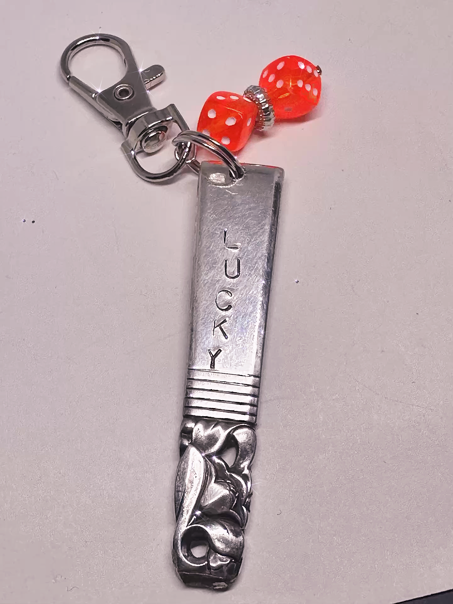 Side view of a Hand-Stamped Lucky Scratch Card Keychain – Upcycled Spoon with Dice Charm, featuring ornate spoon engravings and a striking red dice charm.