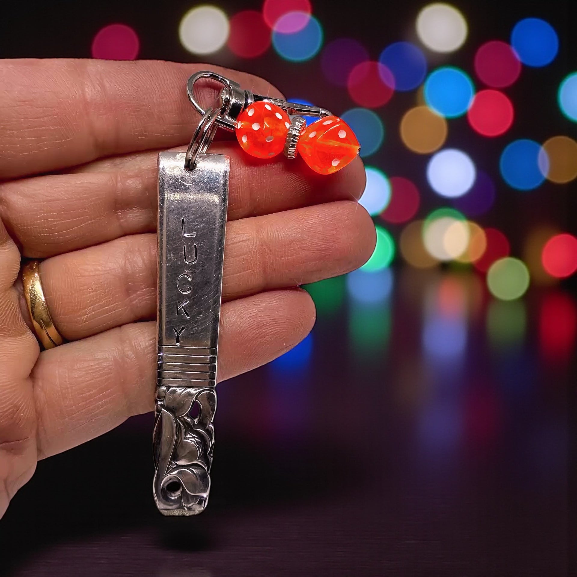 Hand-Stamped Lucky Scratch Card Keychain – Upcycled Spoon with Dice Charm held in hand, featuring a vintage spoon design and red dice charm against a colorful blurred background.