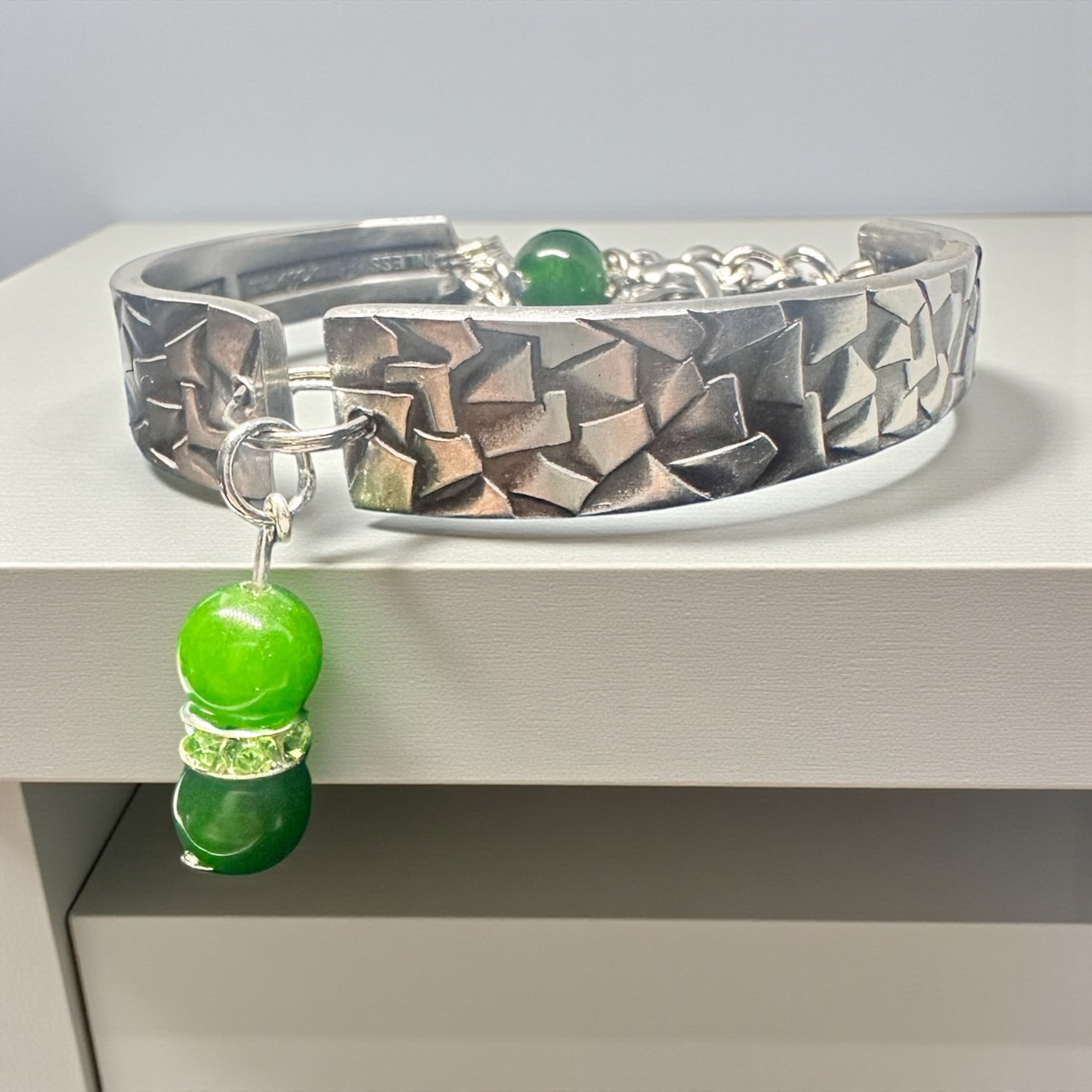 Silver bracelet with green beads on a white surface