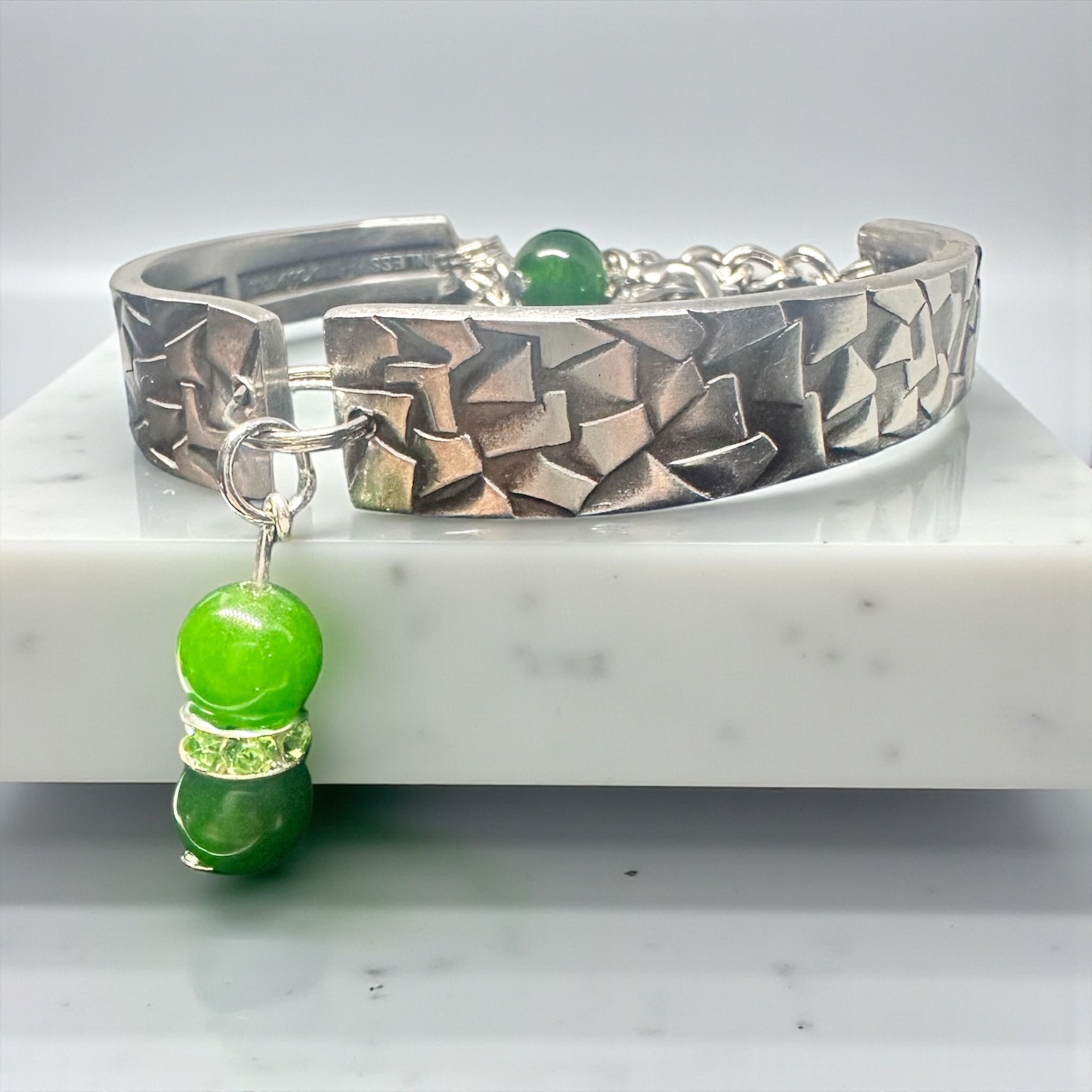 Silver bracelet with geometric pattern and green beads on a marble surface