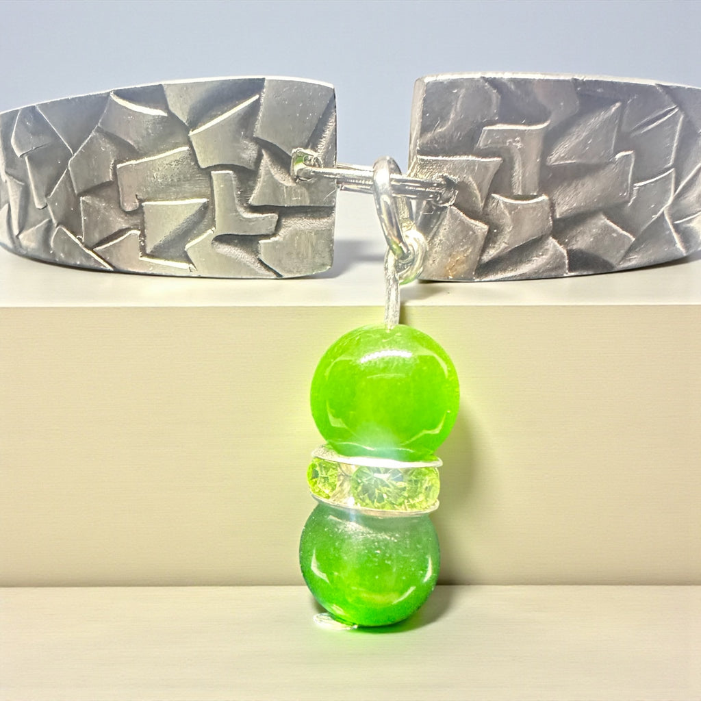 Green beaded earring with textured silver clip on a light gray background