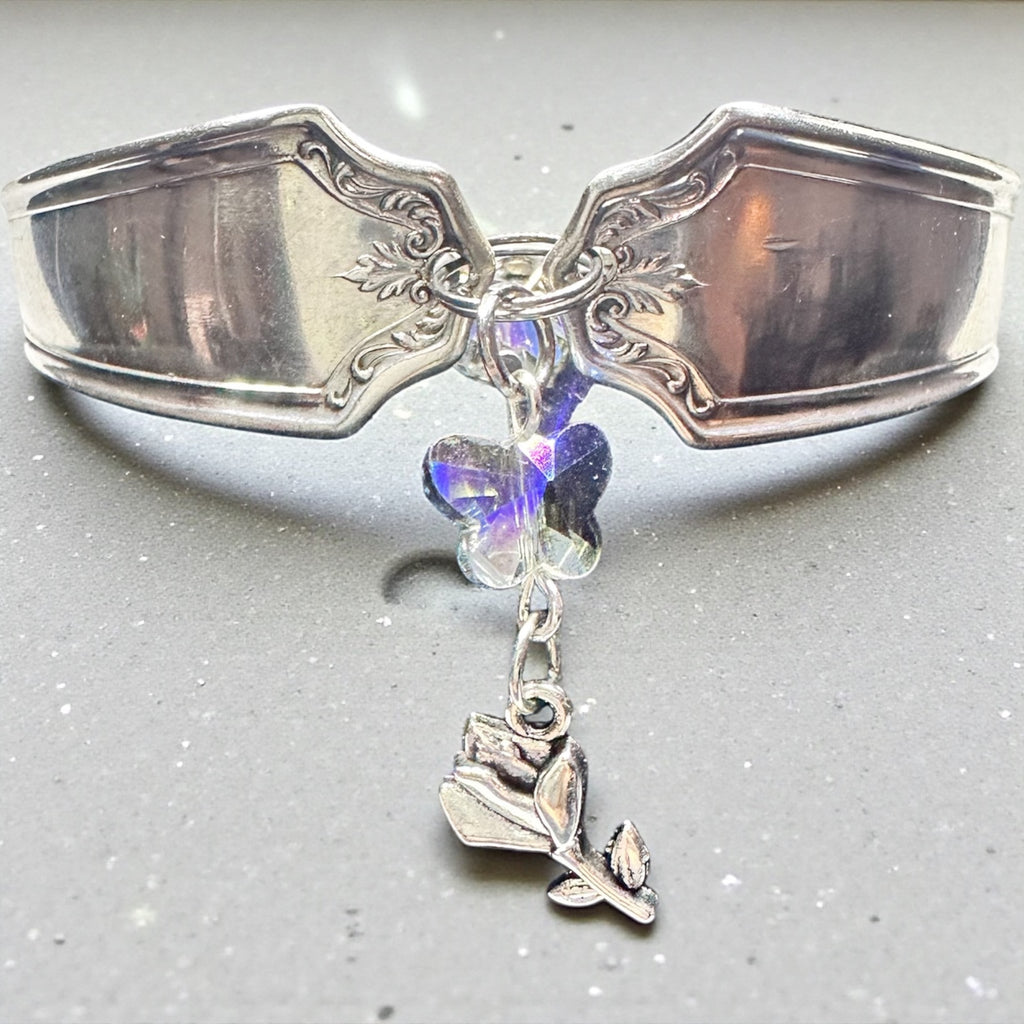Decorative silver spoon with a rose charm and crystal butterfly on a gray background