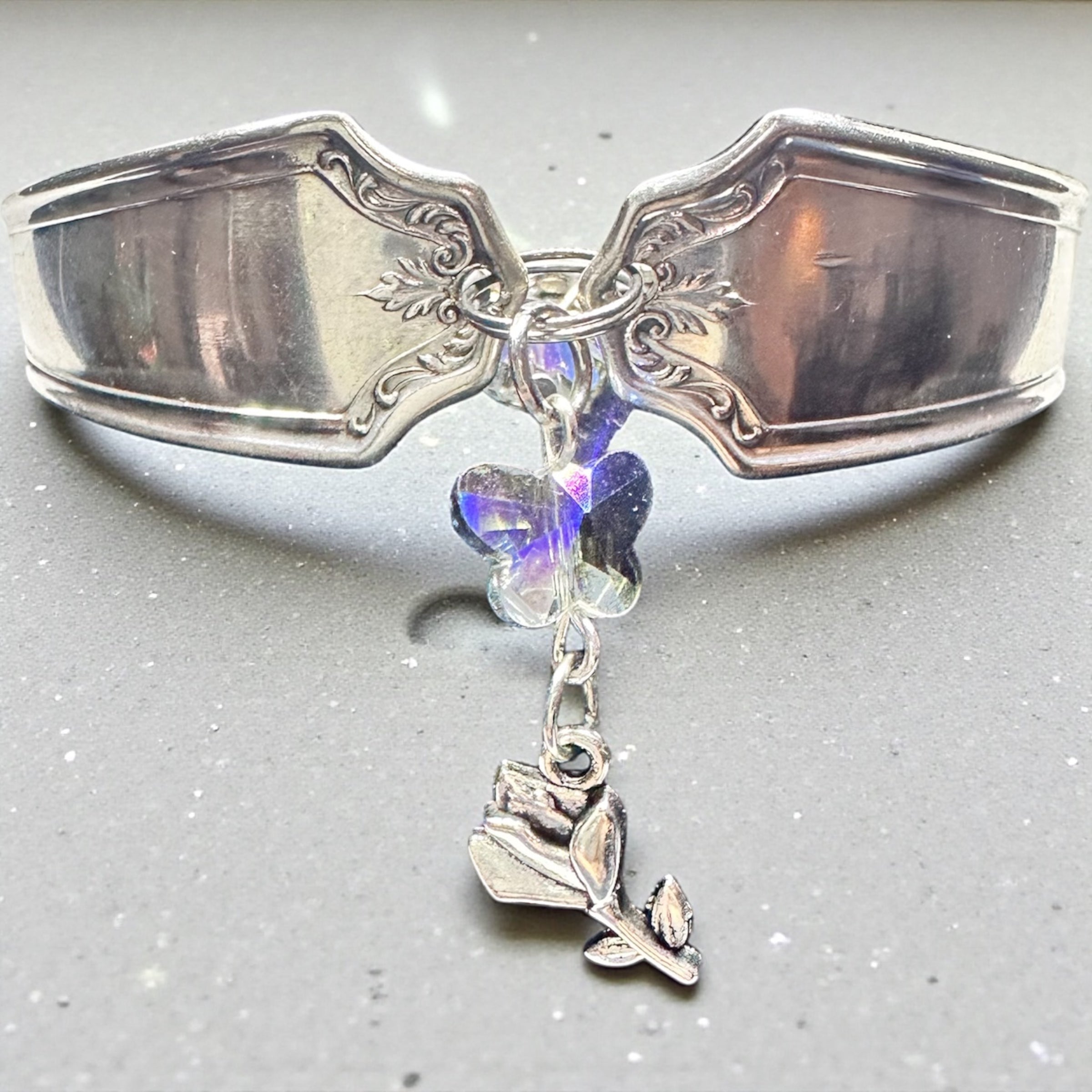 Decorative silver spoon with a rose charm and crystal butterfly on a gray background