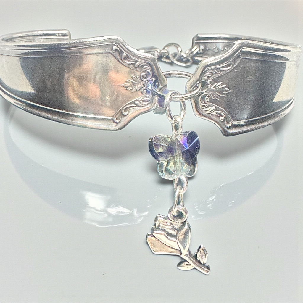 Silver spoon bracelet with butterfly and rose charm on a white background