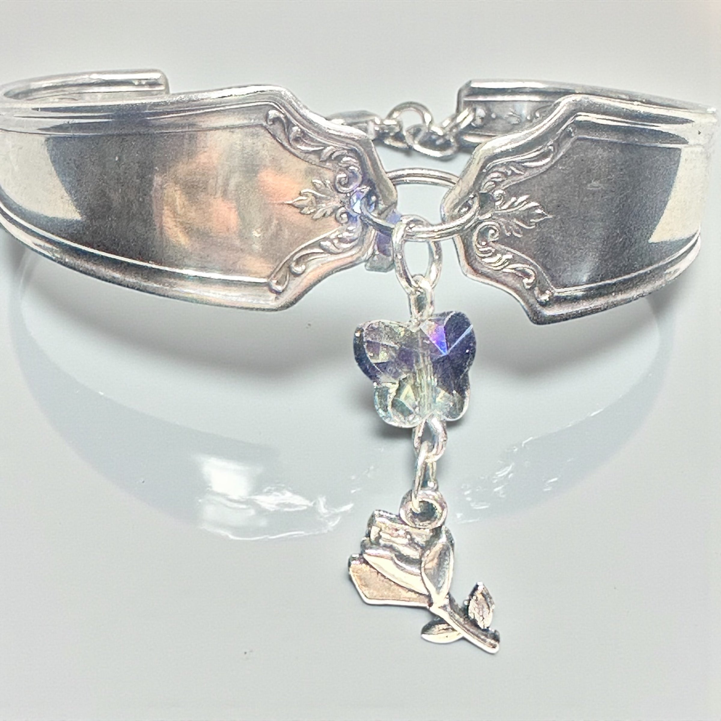 Silver spoon bracelet with butterfly and rose charm on a white background