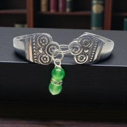 Silver bracelet with green gemstone charm on a black surface